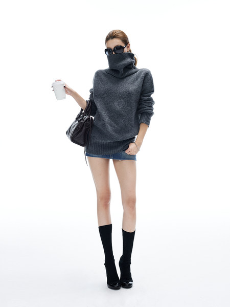 Model wearing a dark gray oversized turtleneck sweater with black boots and a handbag