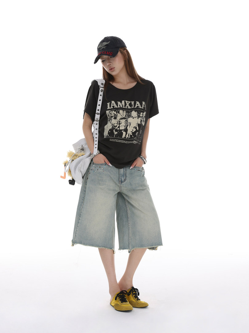 Model wearing a black graphic T-shirt, light denim wide-leg shorts, cap, shoulder bag, and yellow sneakers