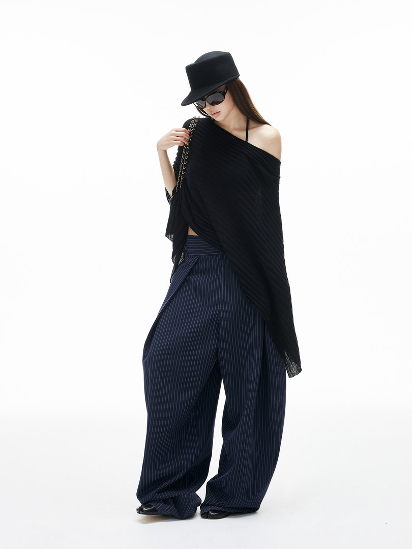 Model wearing a black off-shoulder top with wide pinstripe pants and a black hat