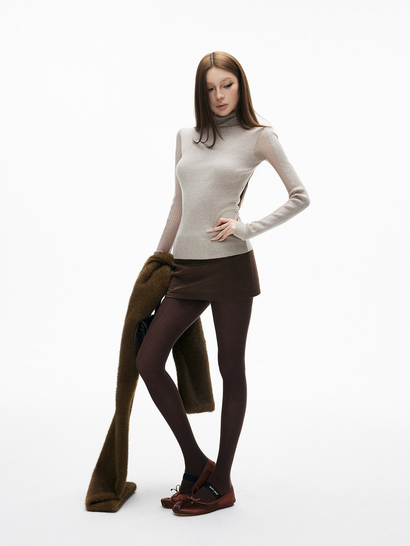 Fashion model wearing a beige ribbed turtleneck top with brown mini skirt, tights, and flats