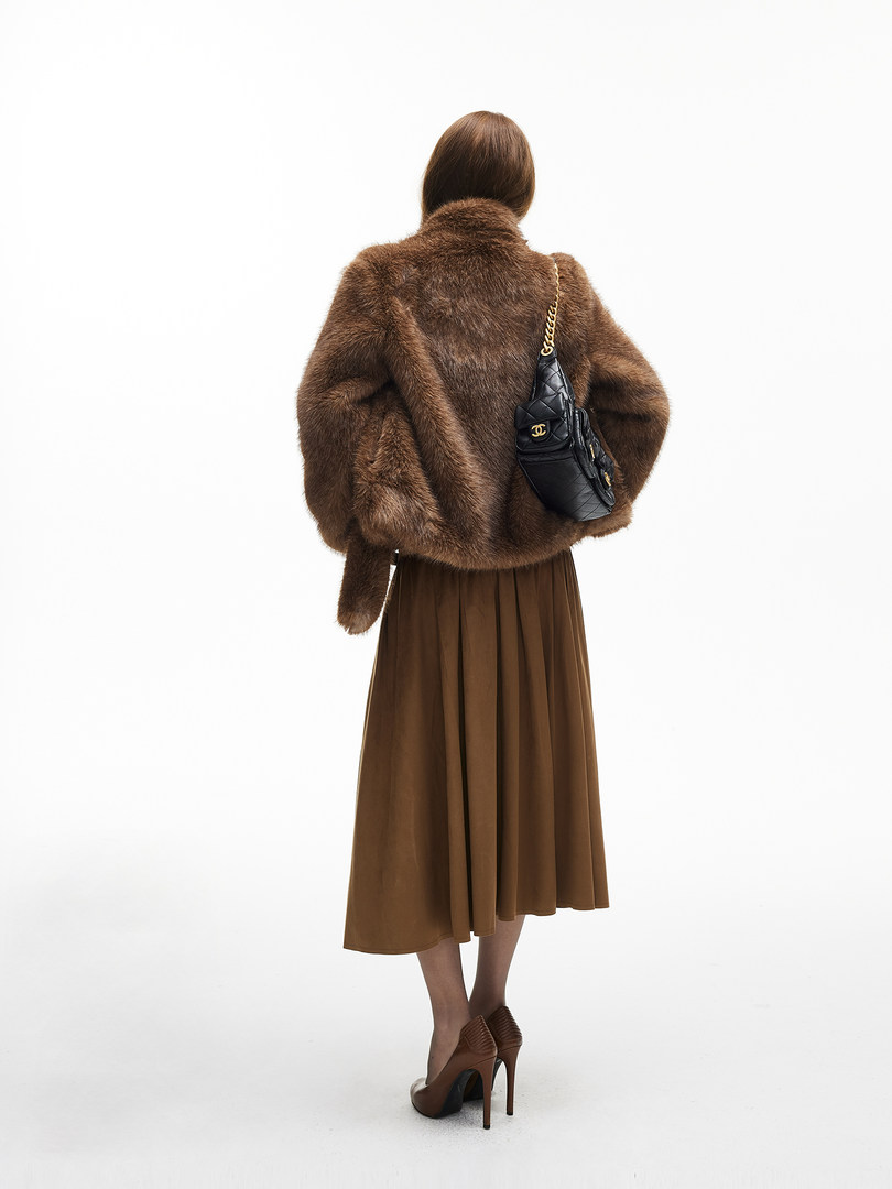 Model wearing a brown faux fur coat, midi skirt, heels, and a black quilted shoulder bag