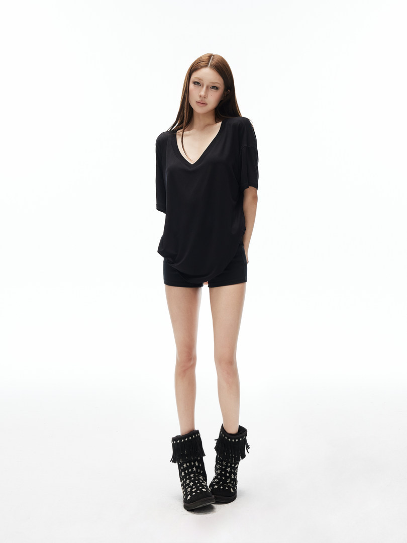 Model wearing a black oversized V-neck top, black shorts, and black fringed studded boots