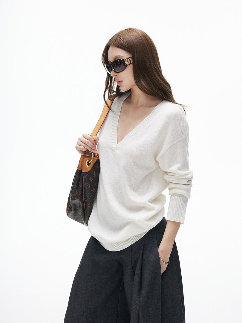 Model wearing a white V-neck sweater with sunglasses and a monogram shoulder bag