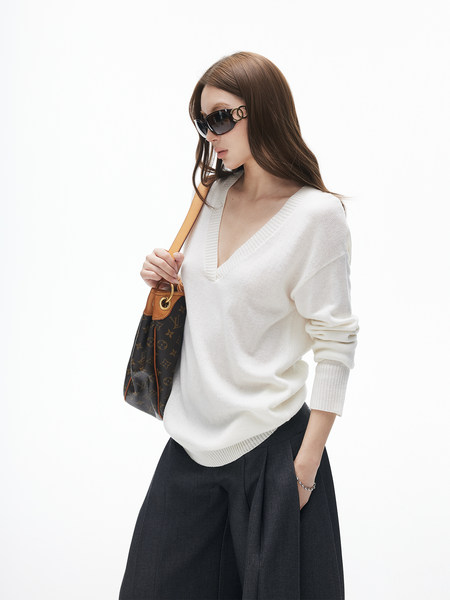 Model wearing a white V-neck sweater with sunglasses and a monogram shoulder bag