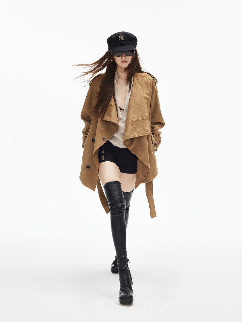 Model wearing a camel trench coat with black thigh-high boots and a black cap on a white background
