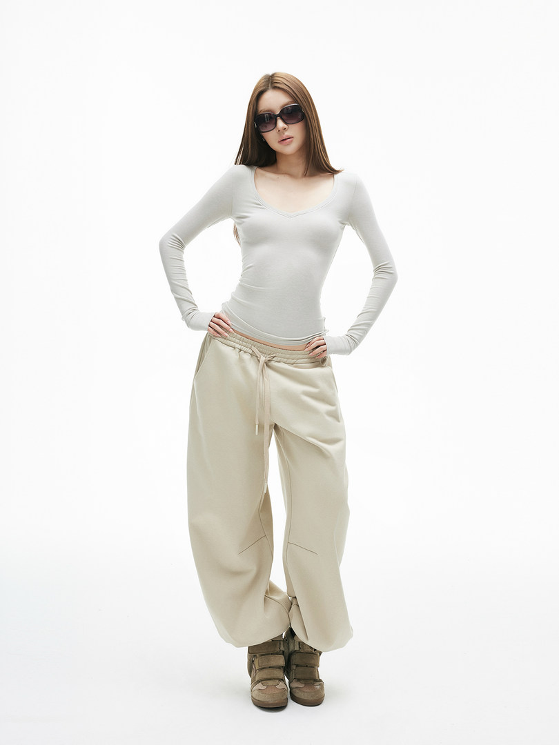 Model wearing a light gray fitted long-sleeve top with beige wide-leg pants and boots