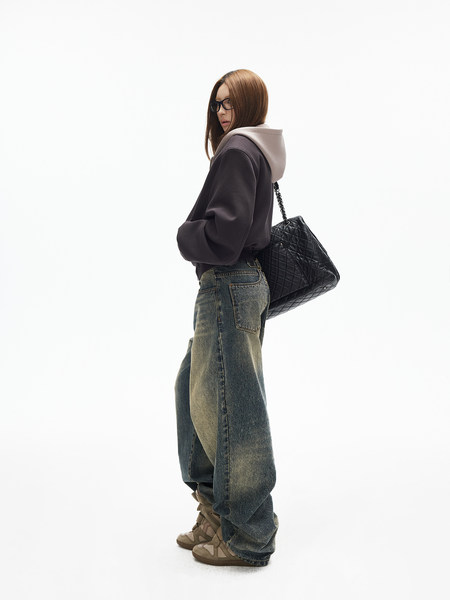 Model wearing oversized hoodie, baggy jeans, sneakers, and a quilted black shoulder bag on a white background
