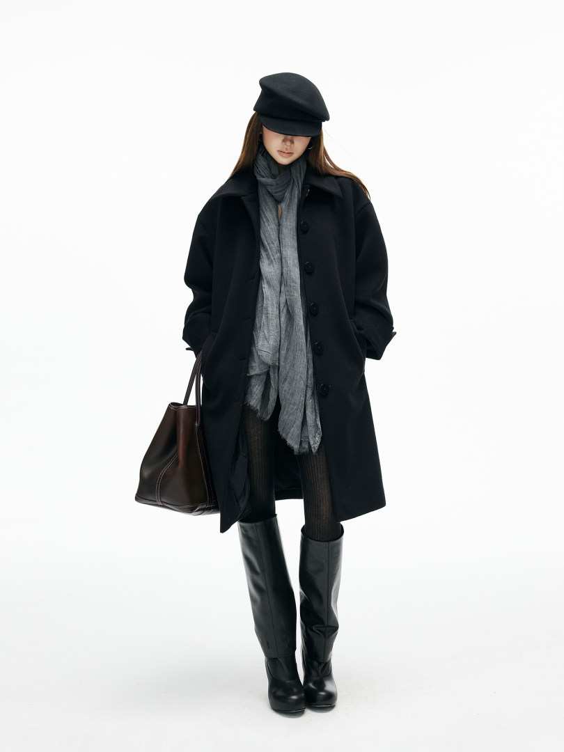 Fashion model wearing a black coat, scarf, hat, boots, and carrying a brown tote bag on a white background