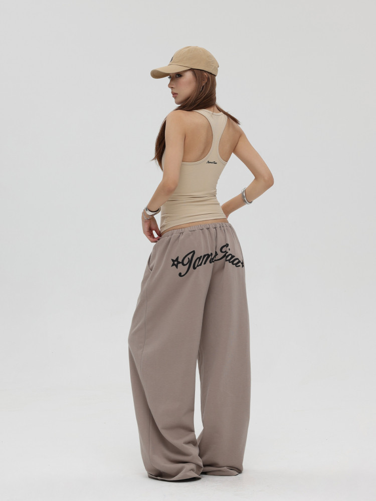 Model wearing a beige tank top, cap, and loose taupe wide-leg pants