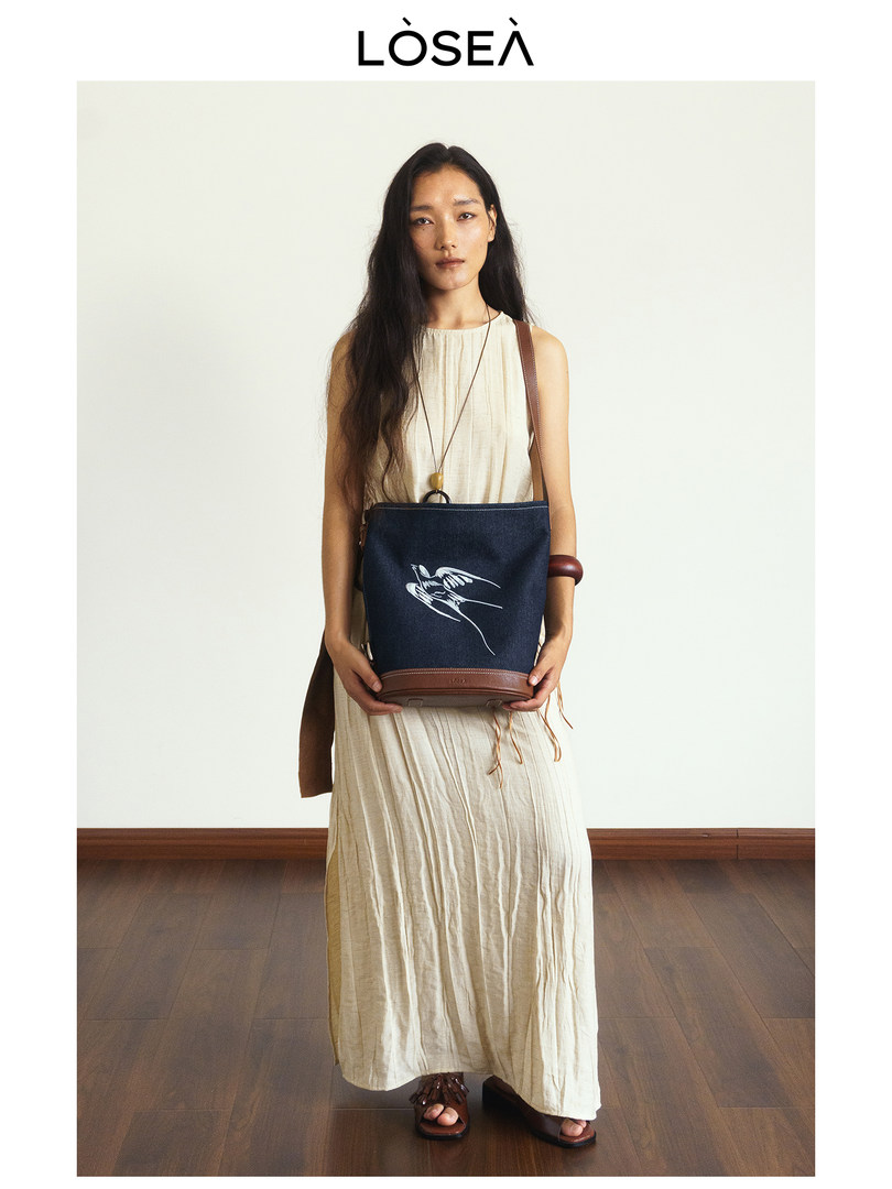Model wearing a cream sleeveless maxi dress and carrying a navy crossbody bag