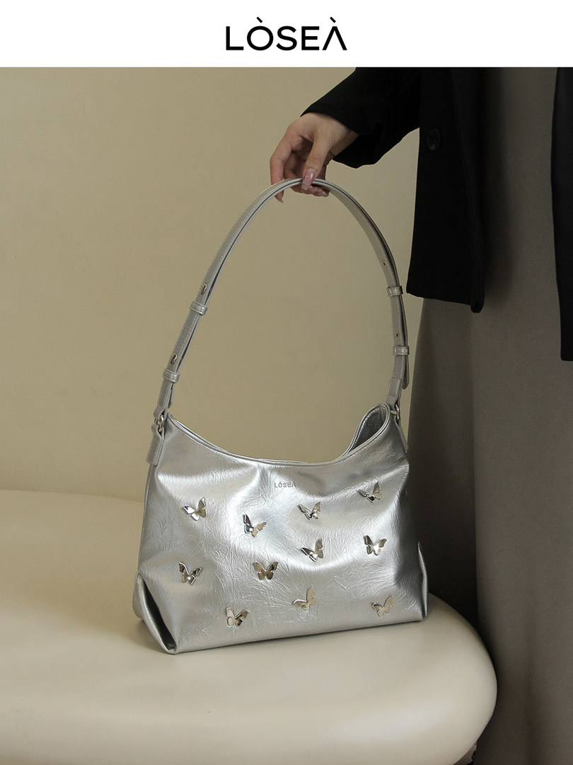 Silver shoulder handbag with butterfly embellishments being held by hand