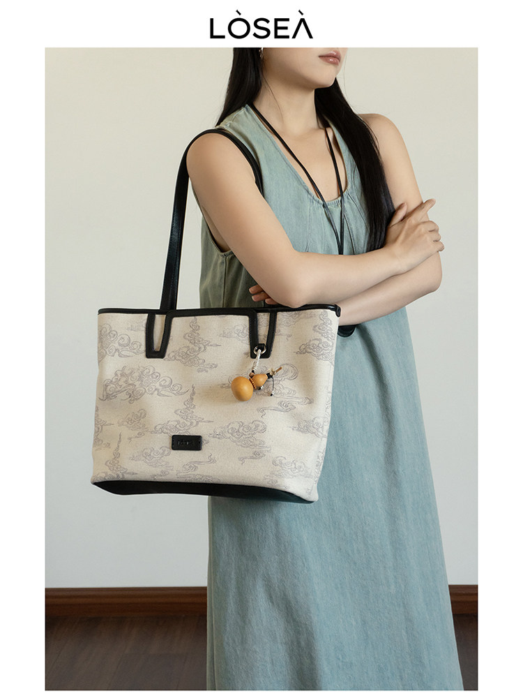 Beige patterned tote bag worn by a model in a sleeveless dress
