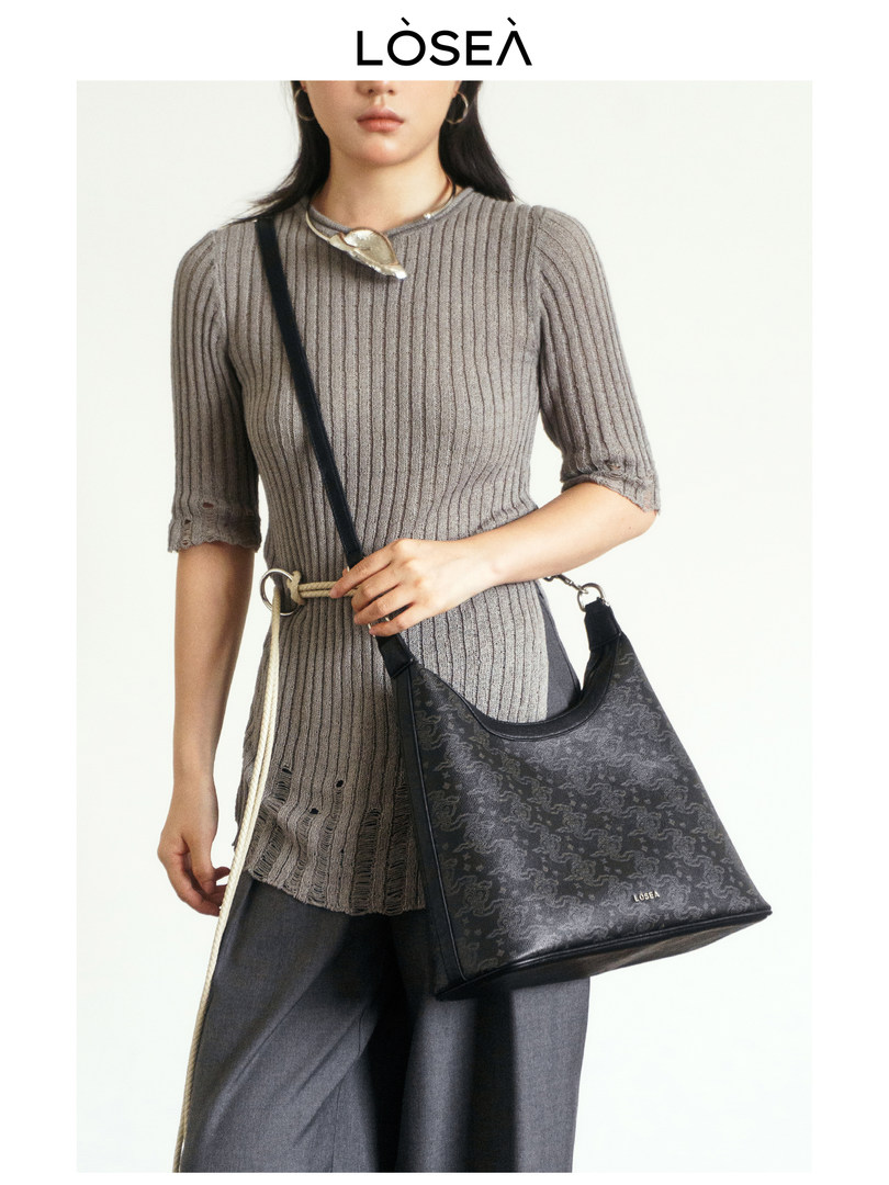 Model wearing a ribbed knit top and carrying a black shoulder bag