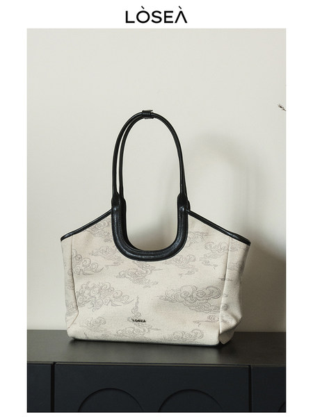 Beige patterned tote handbag with black handles on a white background
