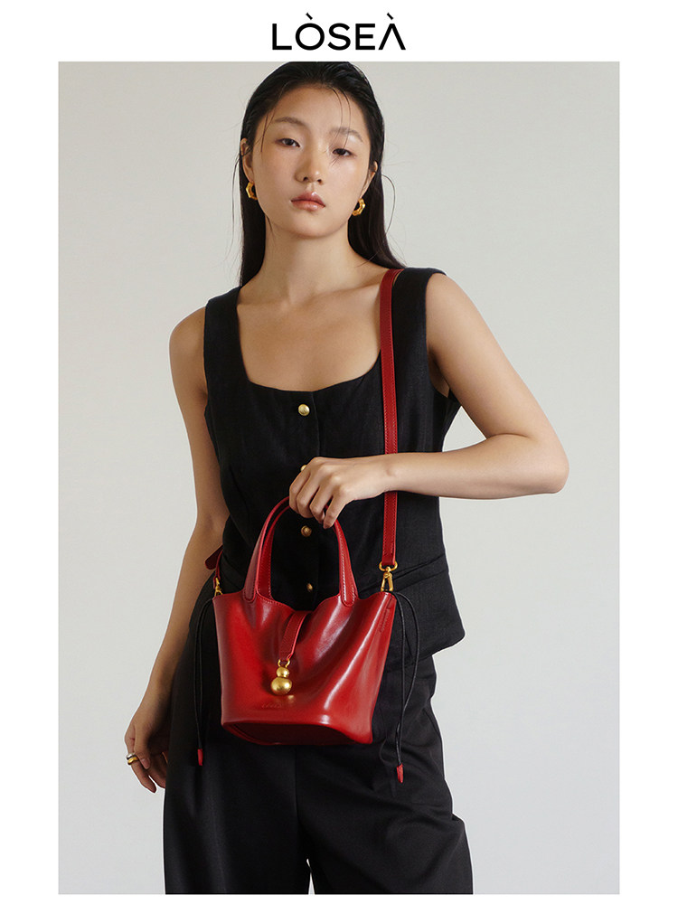 Model wearing a black sleeveless outfit with a red leather handbag