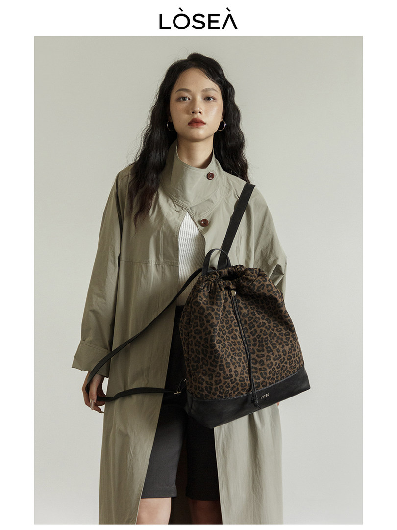 Model wearing an olive trench coat and carrying a leopard print backpack