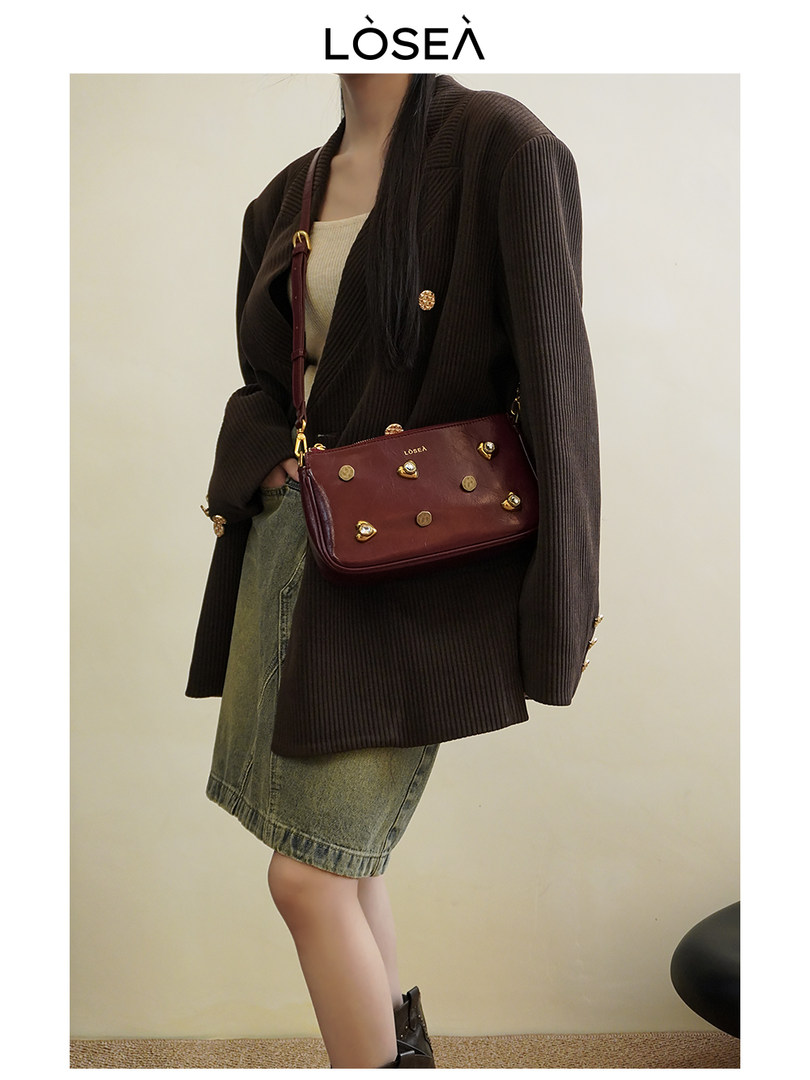 Woman wearing a burgundy crossbody handbag with a dark blazer and denim skirt