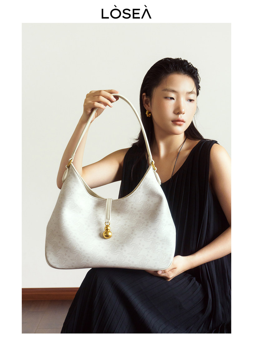 Model holding a white shoulder handbag with gold accent detail
