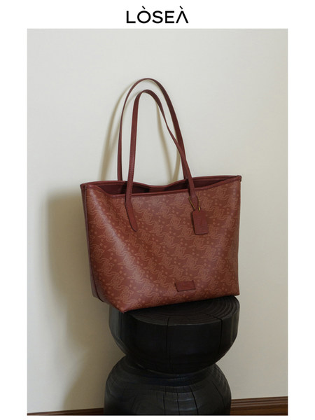Red patterned tote handbag with long handles on a stool