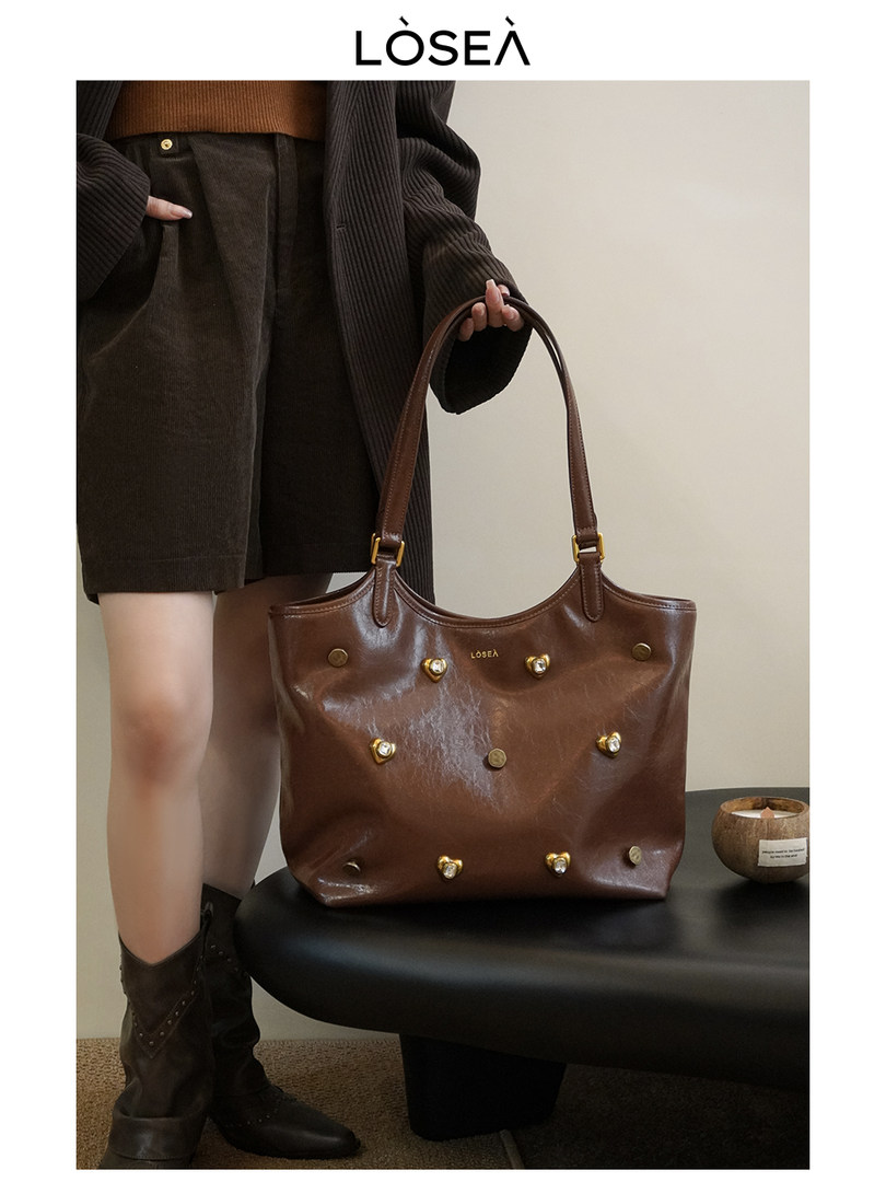 Brown leather tote handbag held by a model wearing a dark fall outfit