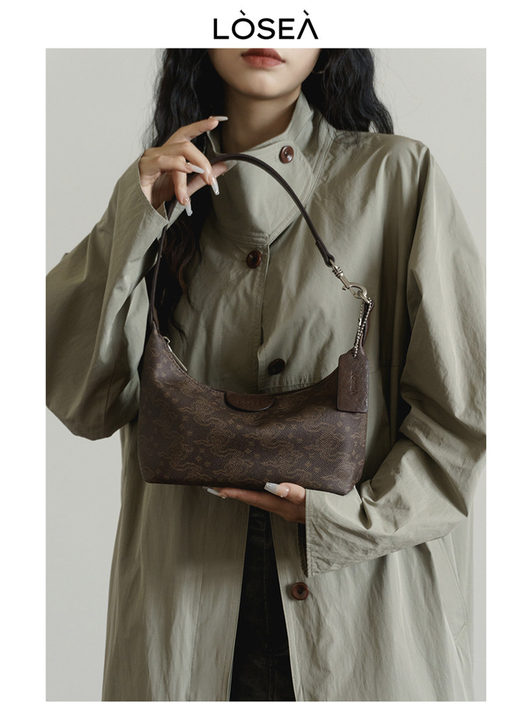 Brown patterned shoulder handbag held by a model wearing a light trench coat