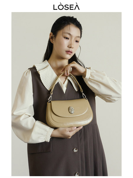 Beige leather handbag held by a model wearing a brown dress and cream blouse