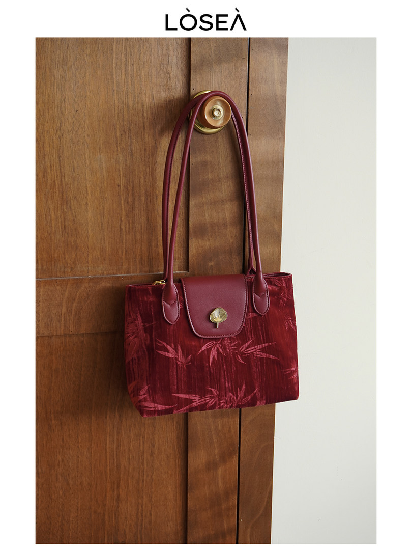 Red velvet shoulder handbag hanging on a wooden door