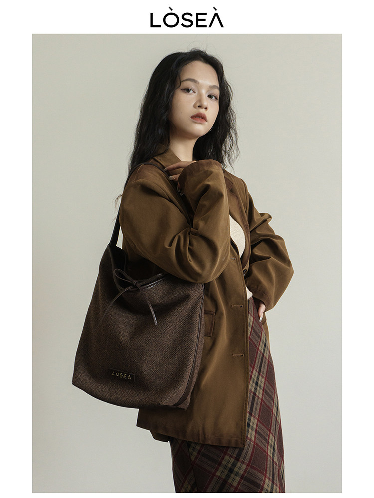 Model wearing a brown blazer and plaid skirt with a dark shoulder bag