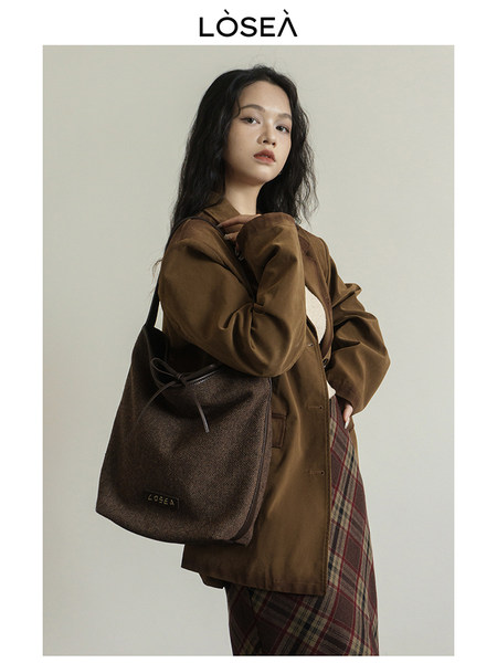 Model wearing a brown blazer and plaid skirt with a dark shoulder bag