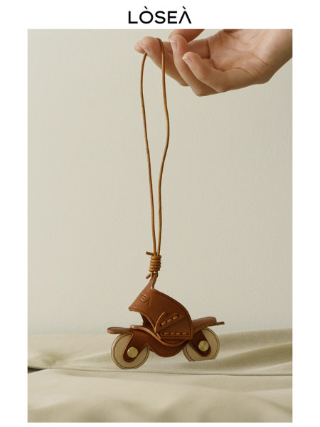 Brown leather scooter-shaped pendant necklace held by hand
