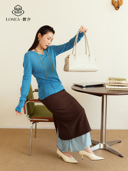 Model holding a white leather handbag in a stylish office-like setting