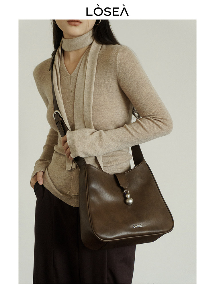 Woman wearing a beige top and scarf with a brown leather shoulder bag