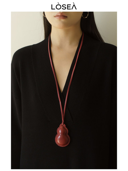 Model wearing a black V-neck top with a red pendant necklace