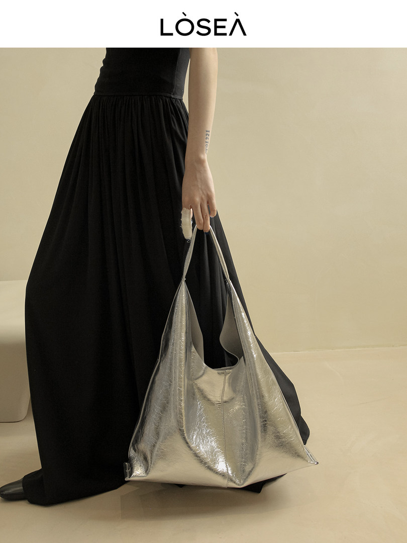 Model wearing a black dress holding a metallic silver oversized tote bag