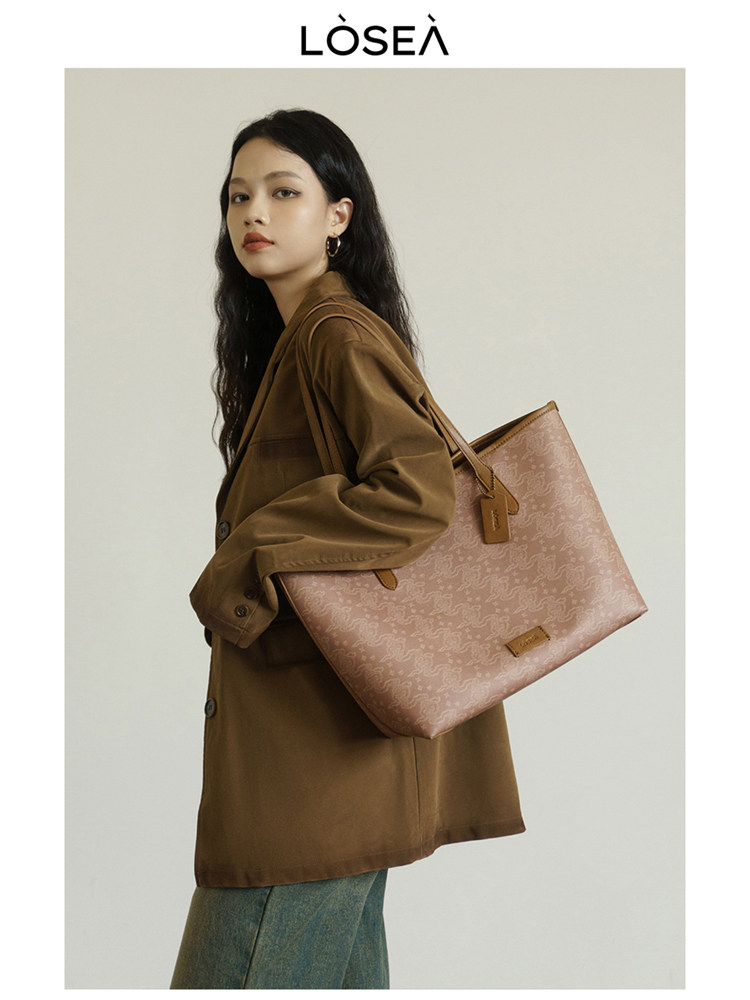 Model wearing a brown coat and carrying a pink patterned tote bag
