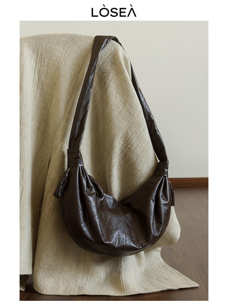 Brown leather shoulder bag displayed on a draped chair