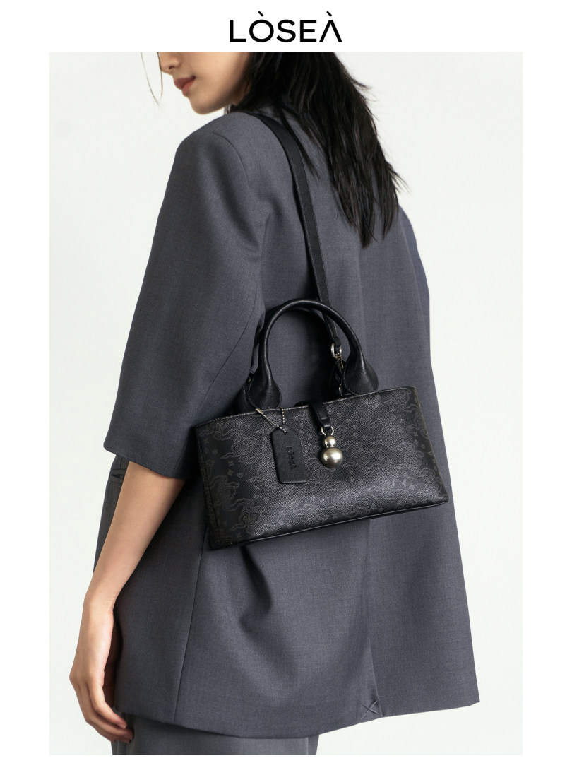 Black structured handbag worn on a model with a gray blazer