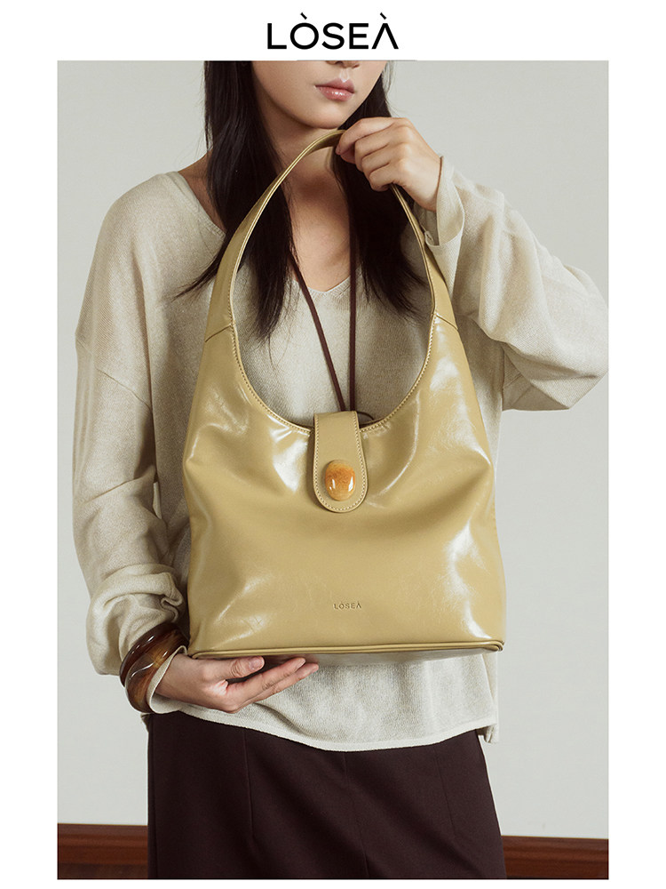 Beige glossy shoulder handbag held by a model
