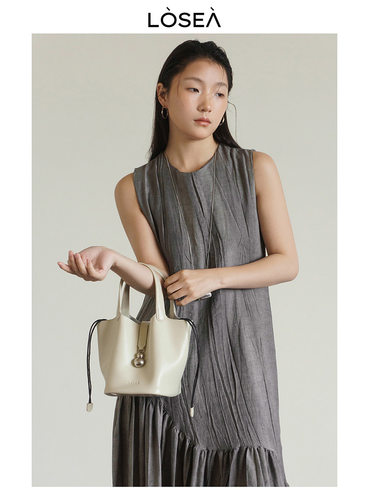 Model wearing a gray sleeveless dress and carrying a cream handbag
