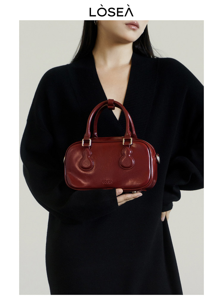 Red leather handbag held by a model wearing a black outfit