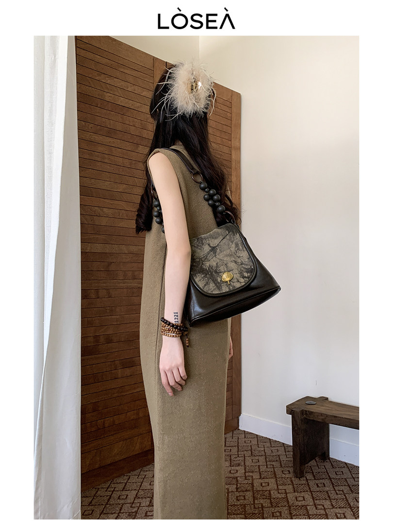 Model wearing a long sleeveless knit dress with a black shoulder bag