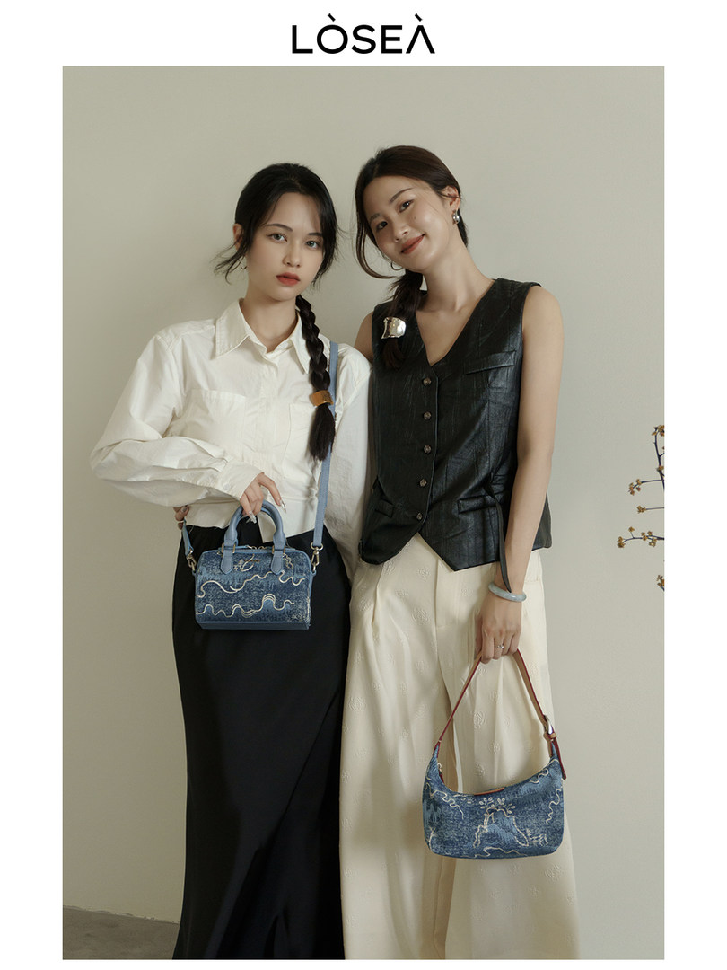 Two women modeling fashion outfits and carrying denim handbags