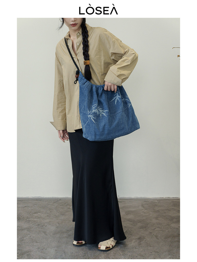 Model wearing a beige oversized shirt, black maxi skirt, and blue shoulder bag