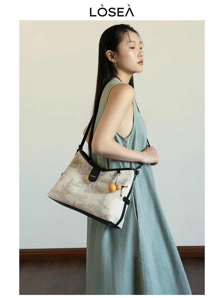 Beige patterned shoulder handbag worn by a model in a sleeveless dress