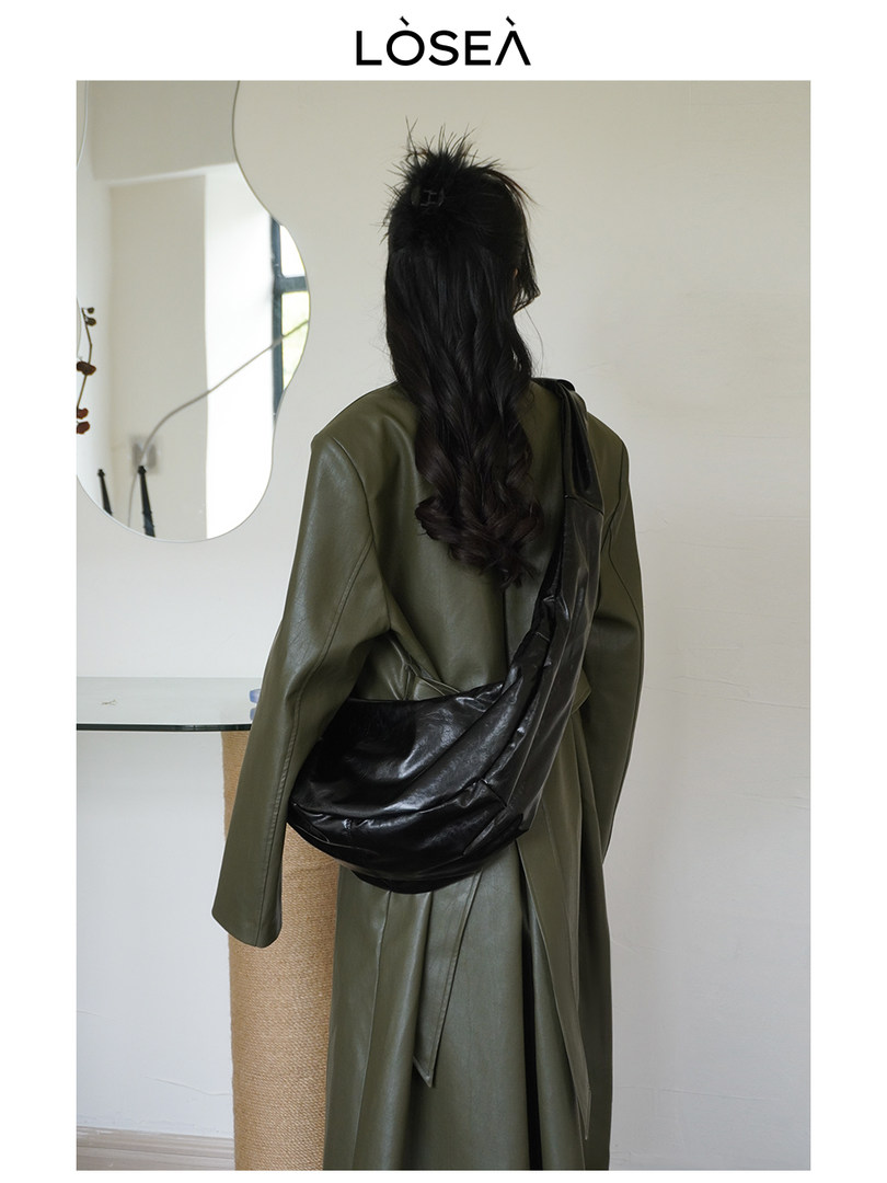 Model wearing an olive green trench coat with a black leather crossbody bag
