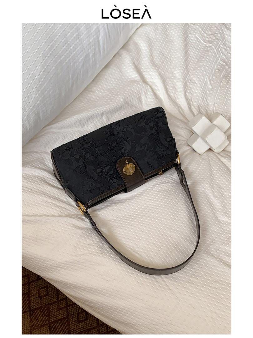 Black patterned shoulder handbag with long strap on a bed