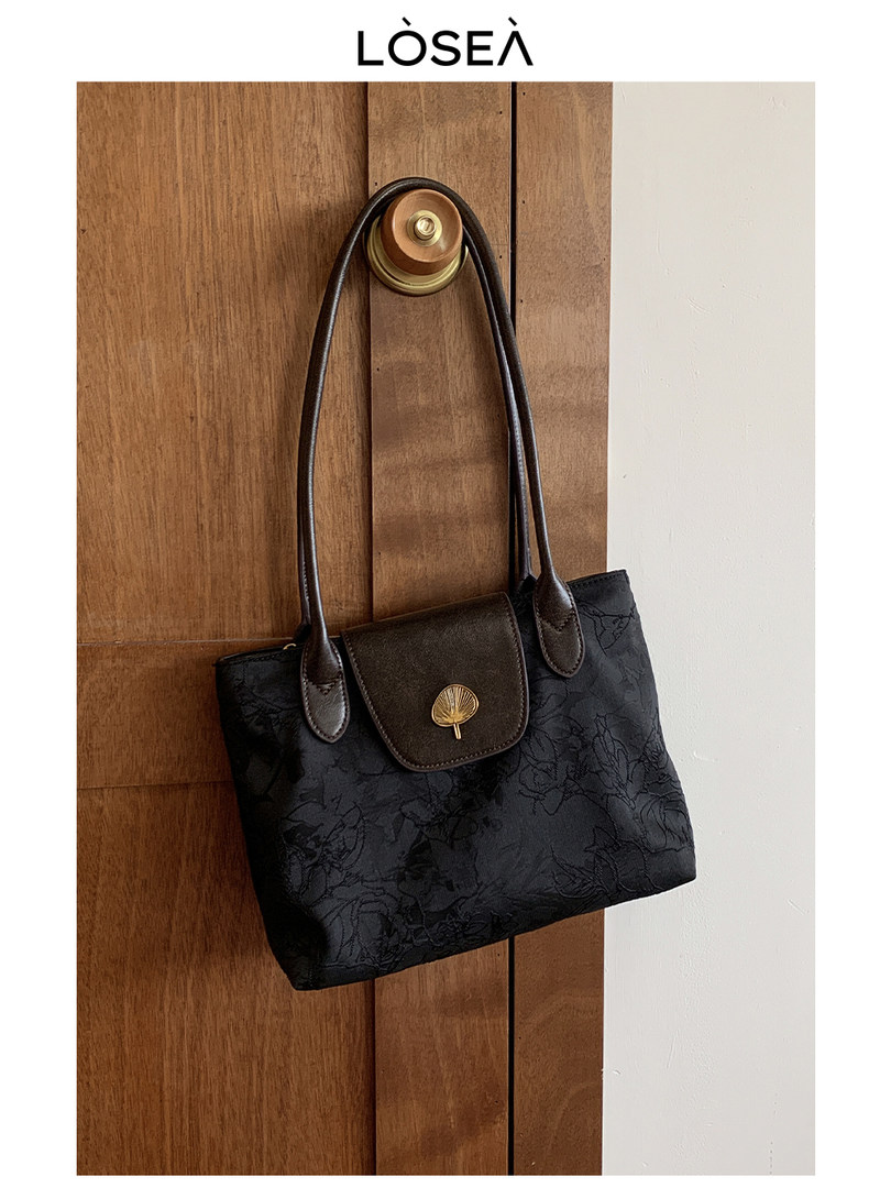 Black patterned tote handbag with long straps hanging on a wooden door