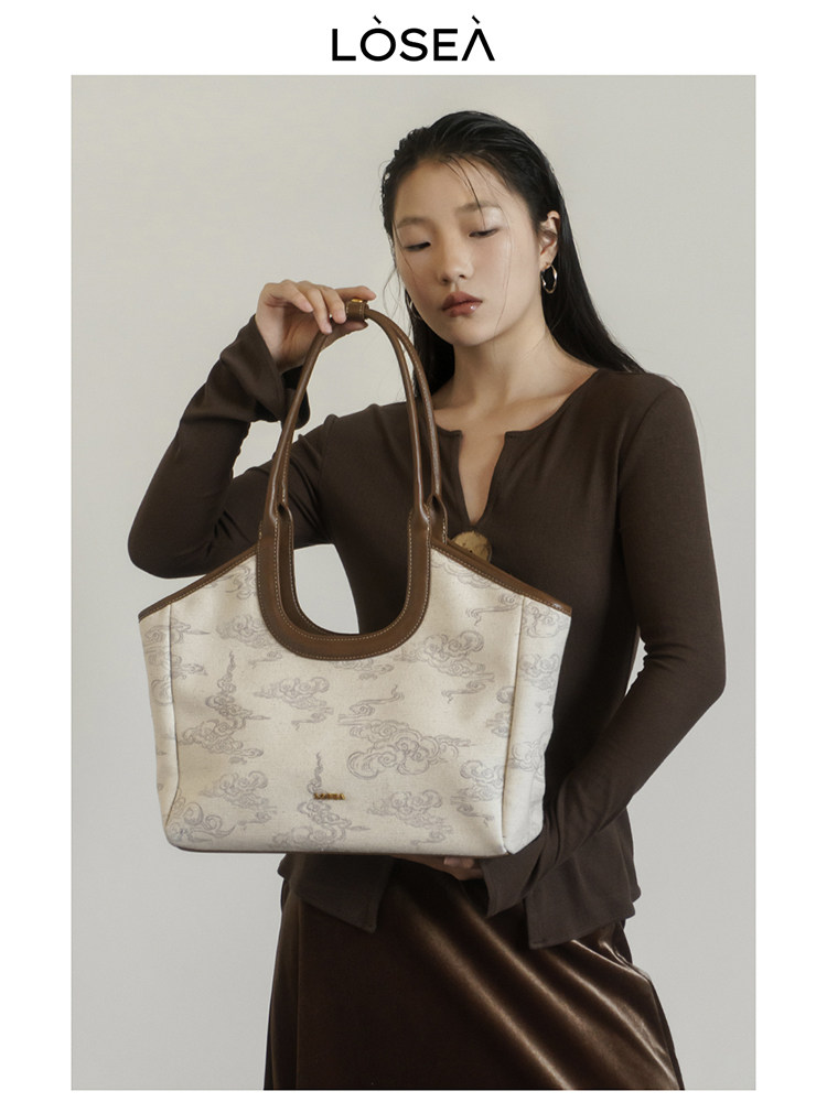 Woman holding a cream patterned tote handbag with brown handles
