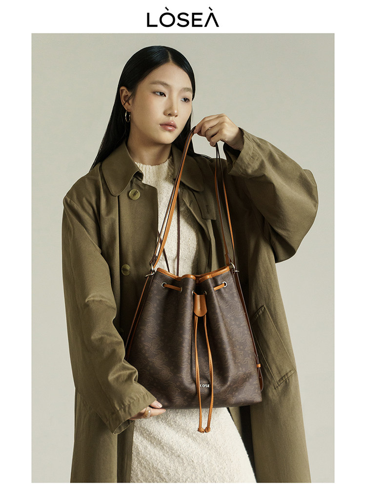 Brown drawstring shoulder bag worn by a model with an olive coat