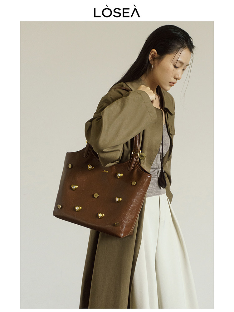 Brown leather tote bag with gold stud details worn by a model